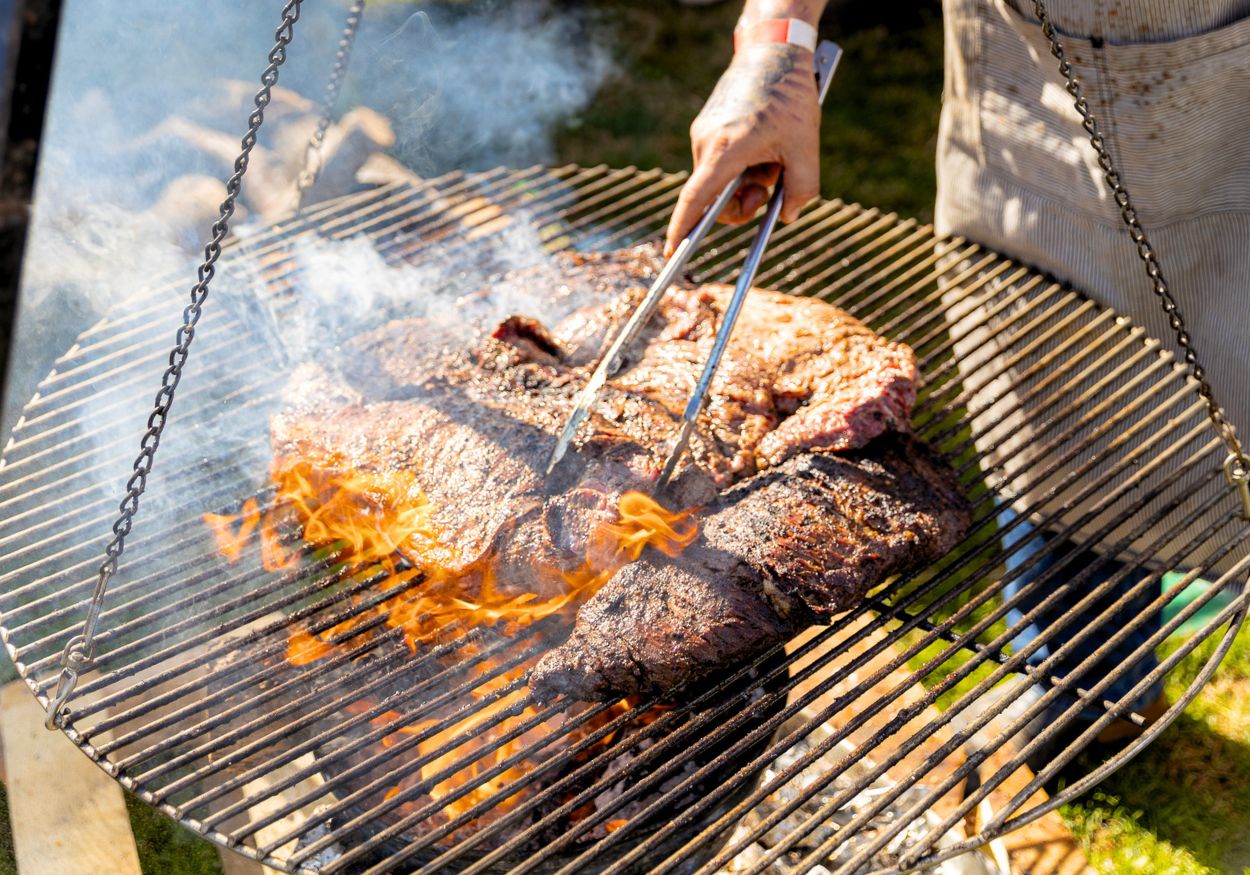 A chef flips steaks over open flames on a live-fire grill